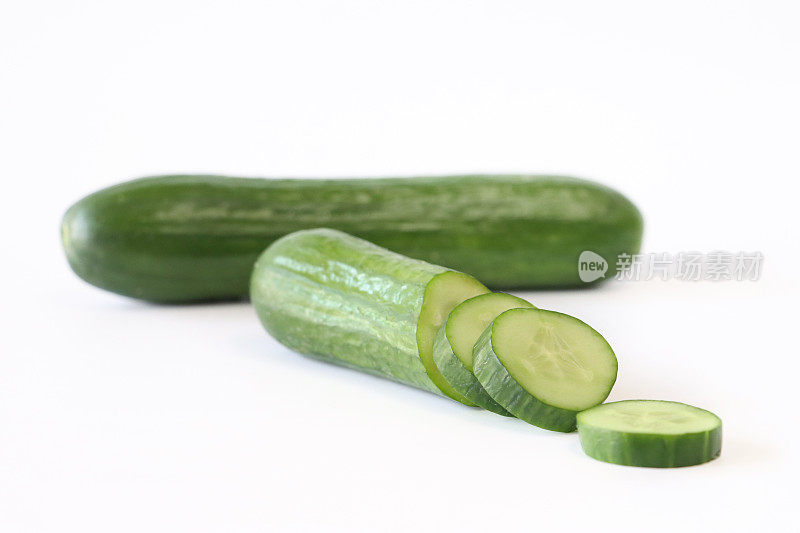 整根黄瓜(Cucumis sativus)和水果切片的特写图像，显示绿色的表皮，白色的果肉和白色的种子，白色的背景，重点在前景